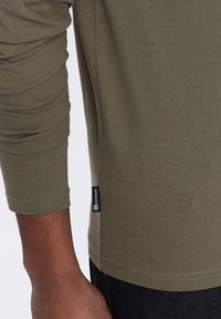Olivgrünes Langarmshirt mit taillierten Ärmeln, Seitennähten und glatter Baumwolltextur. Das Shirt verfügt über einen Rundhalsausschnitt und einen klassischen Schnitt.