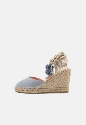 Wedge espadrille with a light gray suede upper, jute rope sole, and multicolored braided ankle ties featuring a pom-pom accent.
