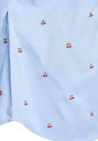 Svetlomodrá košeľa s rozptýlenou červenou výšivkou čerešní so zelenými stonkami, vyrobená z mäkkej látky, zdôrazňujúca hladkú textúru.