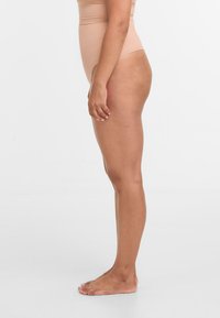 Beige High-Waist-Bodysuit mit einer glatten, dehnbaren Textur; Seitenansicht, die die Passform des Kleidungsstücks auf der Haut zeigt.