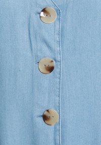 Jasnoniebieska tkanina dżinsowa z czterema okrągłymi, dwuotworowymi guzikami o marmurkowym wzorze, prezentująca gładką, teksturowaną powierzchnię.