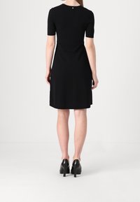 Černé šaty s krátkým rukávem a přiléhavým střihem, jemnou texturou a délkou ke kolenům. Malý knoflíkový detail na zadním výstřihu.