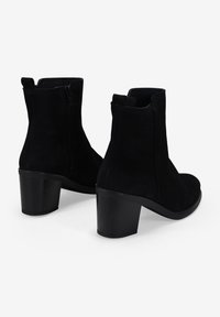 Botines de ante negro hasta el tobillo con un tacón de bloque medio, con cremallera lateral y una textura suave, que ofrecen un diseño limpio y moderno.