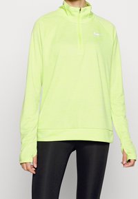 Langärmliger, mit Reißverschluss versehener Pullover aus neongelbem Stoff, der einen hohen Kragen und Daumenlöcher besitzt. Das Design ist glatt mit einer leichten Textur.