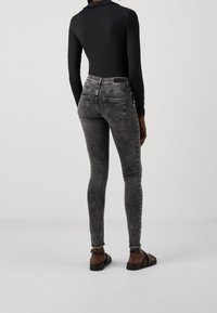 Pantalones ajustados negros desvaídos con cintura alta, cinco bolsillos y dobladillo deshilachado. Combinados con un bodysuit negro de manga larga y sandalias negras.