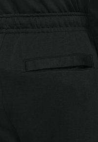 Musta collegehousut pehmeällä pinnalla, joissa on ommeltu taskuyksityiskohta ja joustava vyötärö, joka mahdollistaa säädettävän istuvuuden.