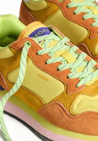 Lace-up sneakers in yellow and orange suede. Featuring green laces, a purple logo, and a textured sole with pink accents.