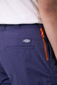 Tamsiai mėlyni šortai su kišenėmis, su užtrauktuku šoninėje kišenėje ir oranžiniu akcentu, tekstūruota medžiaga bei Dickies logotipu ant nugaros.