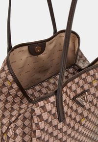 Brązowa torebka z wzorem geometrycznym, wykonana z materiału syntetycznego, z wewnętrzną kieszonką na zamek i akcentem z logo. Górne otwarcie z podwójnymi rączkami.