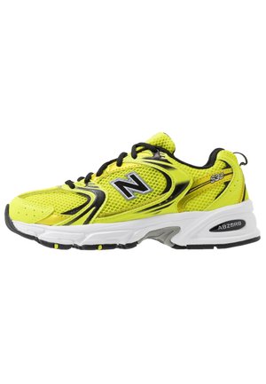 Chaussure de sport New Balance 530 jaune et noire avec empeigne en mesh, semelle blanche et lacets noirs, vue de profil, pied droit.