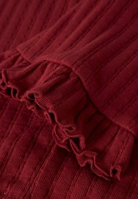 Top de punto burdeos con textura acanalada y un dobladillo con volantes, que muestra un detallado intrincado y un acabado suave.