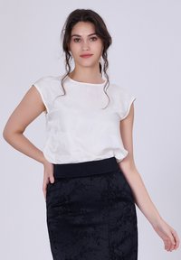 Haut blanc à manches courtes avec un col rond, associé à une jupe crayon noire avec un motif floral texturé et une large ceinture.