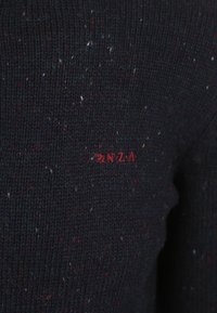 Zwarte gebreide trui met multikleurige stippen. Heeft een klein rood logo dat op de voorkant is gestikt, en toont een gestructureerde stof.