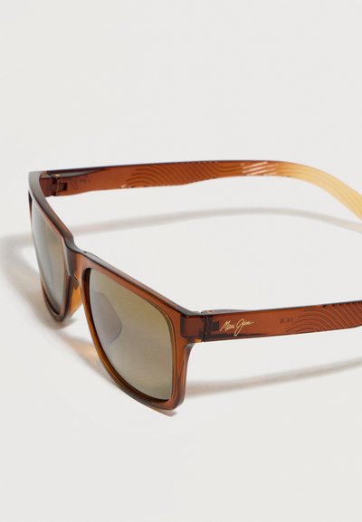 Καφέ διαφανή ορθογώνια γυαλιά ηλίου με σκουρόχρωμους φακούς και διακριτικά κυματιστά μοτίβα στα μπράτσα, τοποθετημένα σε λευκή επιφάνεια.