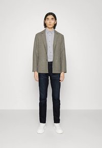 Szürke kockás blézer világosszürke gombos inggel, sötétkék farmernadrággal és fehér tornacipővel. Egyszerű kialakítás, testhezálló szabás.