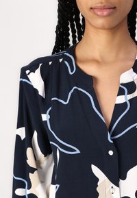 Navy blauwe blouse met een bloemenpatroon in crèmekleurige en lichtblauwe tinten, knoopsluiting en een zachte stoftextuur met een ontspannen pasvorm.