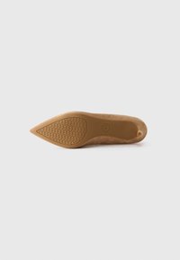 Tan pointed-toe suede flat shoe viewed from the bottom, featuring a textured sole with a circular logo in the center.