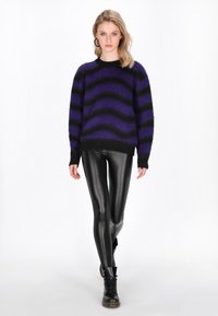 Maglioncino a strisce viola e nere realizzato in materiale morbido, abbinato a leggings neri lucidi e stivali neri. Le strisce presentano un design ondulato.