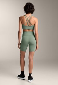 Zelená športová súprava, ktorá obsahuje športovú podprsenku na ramienka a vysoké šortky. Vyrobená z hladkej tkaniny, má priliehavý strih a bezšvový povrch.