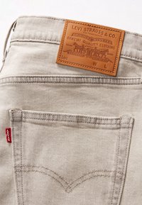 Poche arrière d'un jean Levi's beige clair avec un patch en cuir distinctif de la marque et une étiquette en tissu rouge Levi's visible.