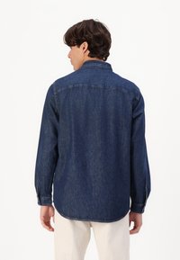 Dark blue denim shirt with a collared neck, long sleeves, and a curved hem. Features simple stitching and button cuffs.