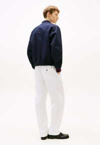 Marine bom jacket met ribbed manchetten en kraag, gecombineerd met witte wijde broek. Ontspannen pasvorm, minimalistisch ontwerp en effen kleuren.