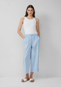 Pantalons larges bleu clair avec une ceinture élastique, associés à un débardeur blanc et des sandales blanches. Tissu lisse avec un minimum de détails.