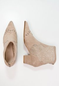 Beige semišové kotníkové boty s květinovým krajkovým vzorem, špičatou špičkou, západním stylem a blokovým podpatkem, zobrazené z horního a bočního pohledu.