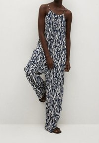 Sleeveless jumpsuit in navy blue and white abstract pattern; lightweight fabric, loose fit, long trousers, and thin shoulder straps.