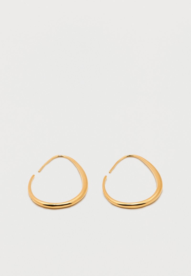 Ζευγάρι λείων, γυαλιστερών σκουλαρικιών σε χρυσό τόνο με ανοικτό κρίκο και ακανόνιστες, οργανικές σταγόνες, σε απλό φωτεινό φόντο.