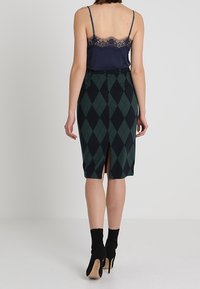 Námořnická tílko s krajkovým lemem v kombinaci se zelenou a černou argyle sukní s tužkovým střihem a rozparkem vzadu. Černé vysoké boty na kotníky.