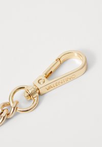 Chiusura in metallo dorato con meccanismo a molla, incisa con "VALENTINO", attaccata a un anello circolare tramite una maglia di catena.