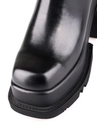 Botte à plateforme noire brillante à bout carré avec semelle en caoutchouc épaisse et détails de couture autour de la zone des orteils.