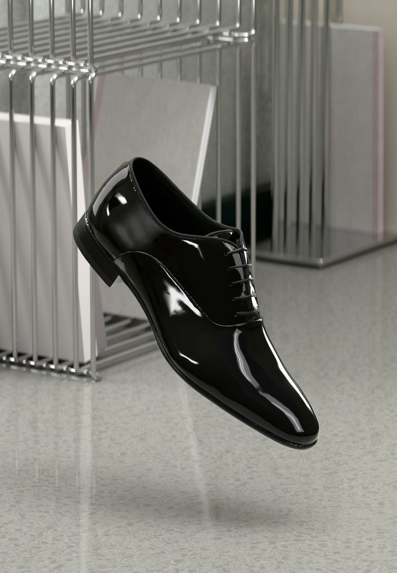 Scarpa elegante in pelle nera lucida appesa a un ripiano metallico sopra un pavimento liscio di colore chiaro.