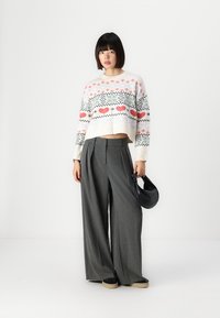 Crochet sweater with multicolored pattern, cropped design, paired with gray wide-leg trousers and a small black handbag.