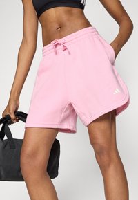 Rózsaszín sportnadrág puha anyagból, gumis derékrésszel és húzózsinórral, oldalzsebekkel és fehér Adidas logóval díszítve.