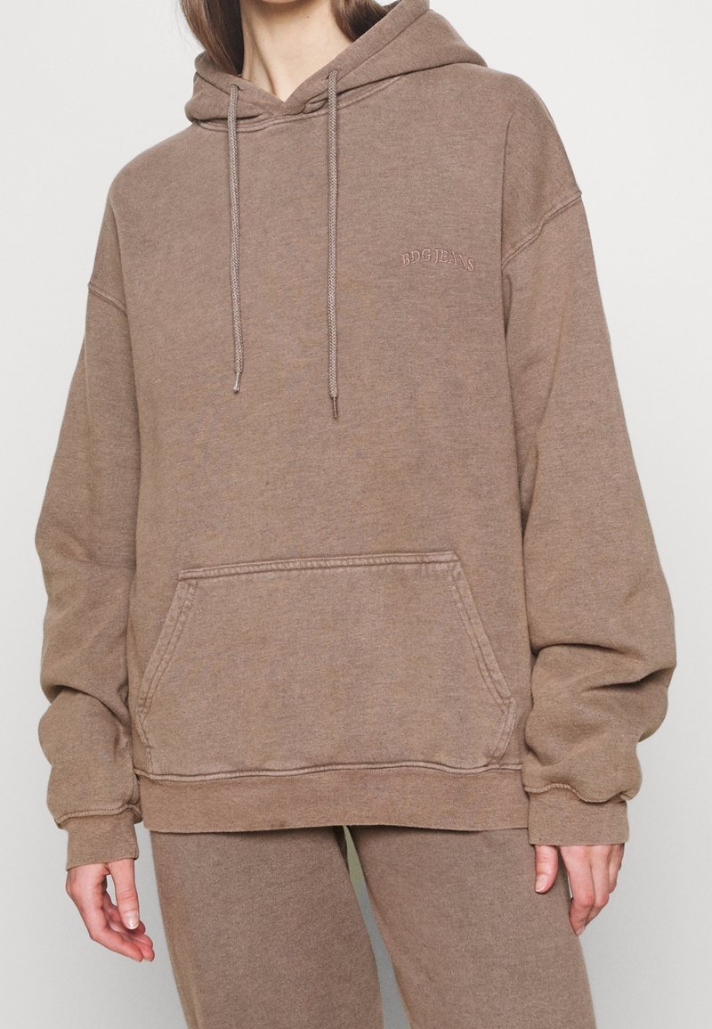 Felpa marrone oversize in tessuto morbido, con tasca frontale a marsupio, cappuccio con coulisse e logo ricamato discreto sul petto.