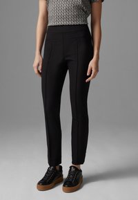 Pantalons slim-fit noirs avec deux poches avant, associés à des baskets noires épaisses avec une semelle en caoutchouc et des œillets dorés.
