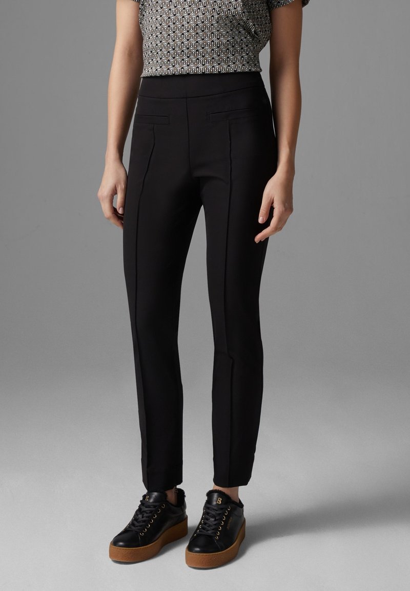 Pantalons slim-fit noirs avec deux poches avant, associés à des baskets noires épaisses avec une semelle en caoutchouc et des œillets dorés.
