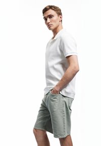 Weißes geripptes Poloshirt und hellgrüne Shorts mit Taschen. Die Shorts haben einen lässigen Schnitt und das Shirt hat einen klassischen Kragen.