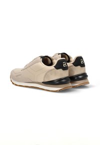 Zapatillas deportivas beige con texturas de ante y cuero, acentos en el talón negros, entresuela blanca y suela de goma. Forma redondeada con un diseño minimalista.