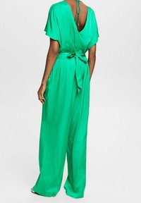 Monos de color verde, hechos de un material ligero, con un profundo escote en la espalda, mangas cortas, una cintura ajustada con un lazo y pantalones de pierna ancha.