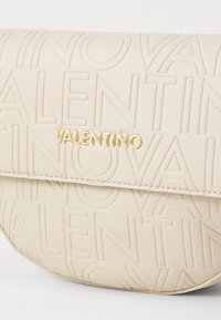 Béžové kožené psaníčko s vyraženým logem VALENTINO, zlatými kovovými doplňky a hladkou texturou. Má zakřivený tvar a jemné šití.