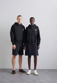 Black hooded sweatshirts with front pockets, paired with black shorts and a skirt. Notable yellow smiley logo on each sweatshirt.