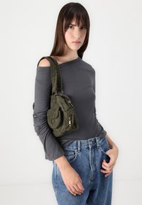 Top gris de manga larga con diseño descubierto en los hombros, combinado con unos jeans de mezclilla azul de tiro alto. Bolso de pana verde oliva con bolsillos.