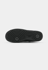 Sola de ténis de borracha preta com padrões texturizados circulares e em ondas, apresentando dois acentos de borracha circulares e o logo da Nike.