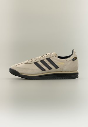 Baskets Adidas SL 72 beige avec des bandes noires, semelle noire et étiquette en tissu Cordura au talon, présentées de profil sur fond clair.