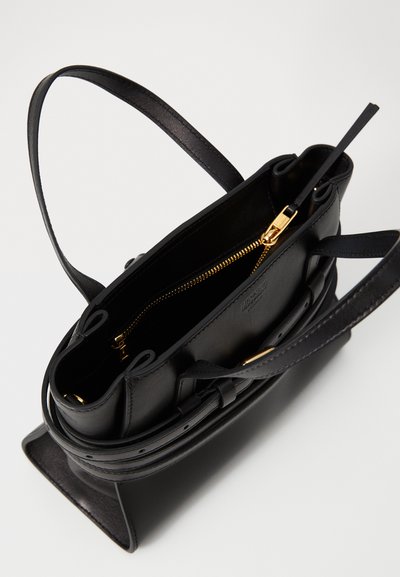 Sac à main en cuir noir avec fermeture éclair, quincaillerie dorée et une seule bandoulière. Il a une forme structurée avec des poches intérieures.