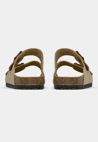 Rjav open-back natikače z dvema nastavljivima trakovoma, teksturiranimi korkovimi vložki, ravnim črnim gumijastim podplatom in gladkim usnjem zgoraj.