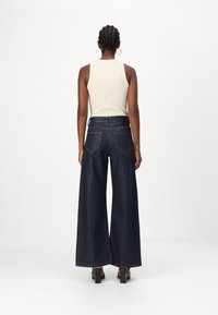 Weite Denim-Jeans in dunklem Indigo, mit hoher Taille, zwei Gesäßtaschen und einer glatten Textur. Kombiniert mit einem figurbetonten Creme-Top.